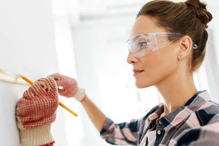 woman with ruler and pencil measuring wall at homeの写真素材