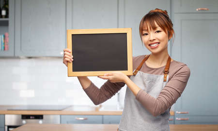 happy woman in apron with chalkboard in kitchenの写真素材