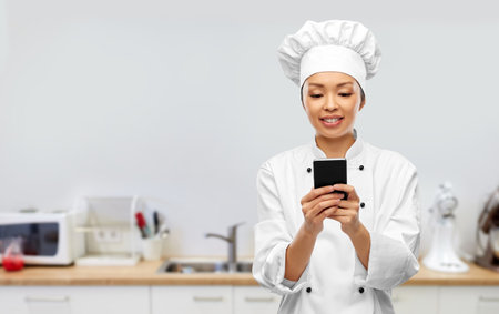 smiling female chef with smartphone in kitchenの写真素材