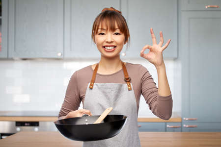 woman in apron with frying pan shows ok in kitchenの写真素材