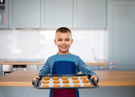 boy in apron holding baking tray with cookiesの写真素材