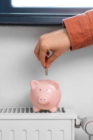 hand putting coin into piggy bank on radiatorの写真素材