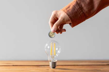 close up of hand with coin and lightbulb on table