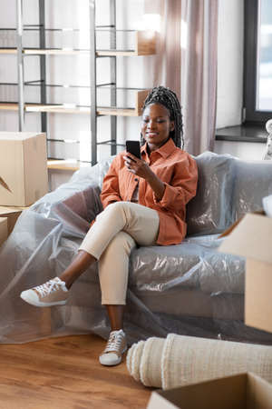 woman with smartphone and boxes moving to new home