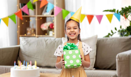 happy girl in party hat with birthday gift at homeの写真素材