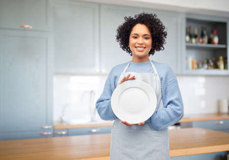 smiling woman holding clean empty plate in kitchenの写真素材