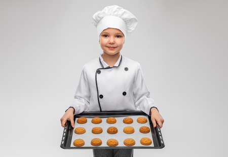 boy in toque holding baking tray with cookiesの写真素材