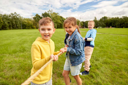 happy children playing tug-of-war game at parkの写真素材
