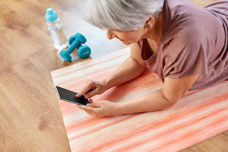 senior woman with smartphone exercising at home