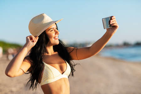 smiling woman in bikini taking selfie on beachの写真素材