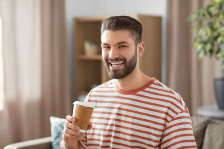 smiling man drinking takeaway coffee at homeの写真素材
