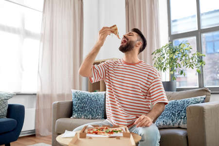 happy man eating takeaway pizza at homeの写真素材
