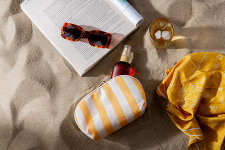 magazine, sunglasses and sunscreen on beach sand