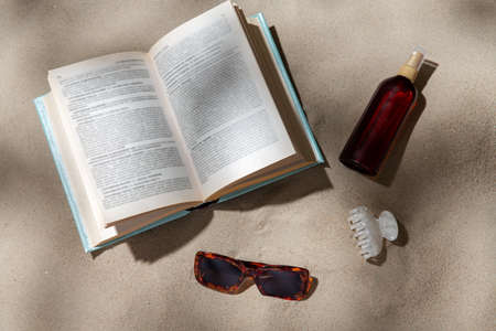 book, sunglasses and sunscreen on beach sandの写真素材
