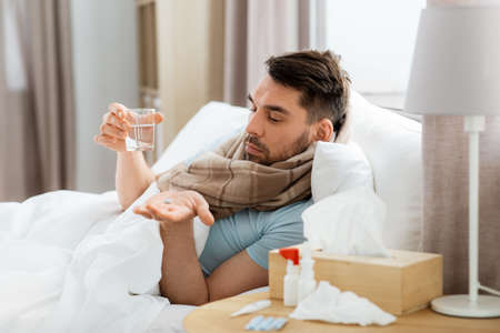 sick man with medicine and water in bed at homeの写真素材