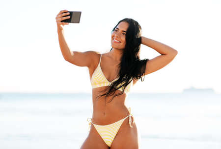 smiling woman in bikini taking selfie on beachの写真素材