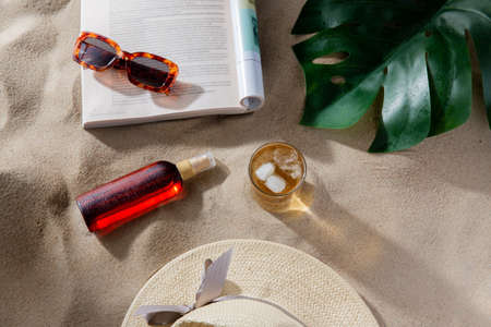 magazine, sunglasses and sunscreen on beach sand