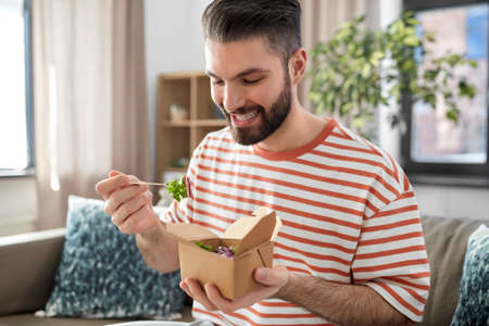smiling man eating takeaway food at home