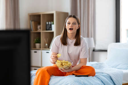 happy girl eating crisps and watching tv at homeの写真素材