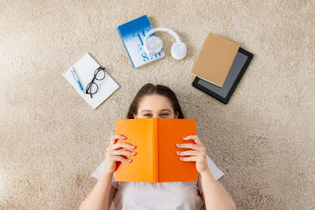 happy student girl with book and gadgets on floor