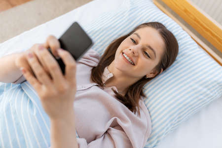 happy girl with smartphone in bed at home