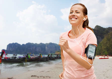 woman with earphones add armband jogging on beach