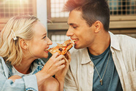 happy couple eating pizza outdoors