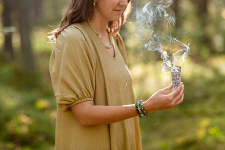 woman with sage performing magic ritual in forest