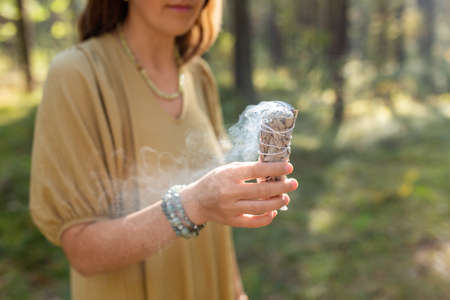 woman with sage performing magic ritual in forest