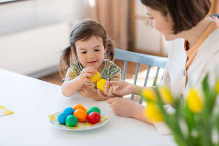 baby girl and mother tapping easter eggs at home