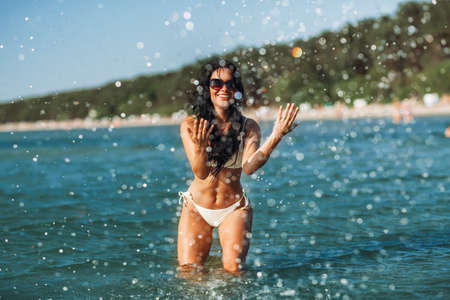 woman in bikini splashing sea water on beach