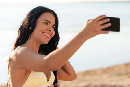 smiling woman in bikini taking selfie on beachの写真素材