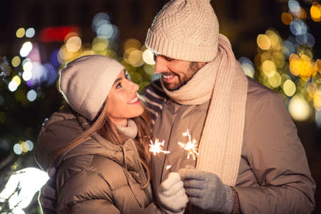 happy couple with sparklers over christmas lightsの写真素材