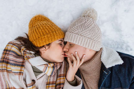 happy couple kissing lying on snow in winterの写真素材