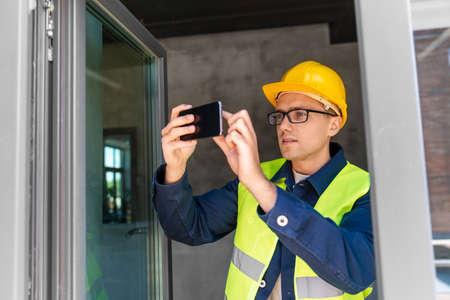 builder with smartphone taking picture at window