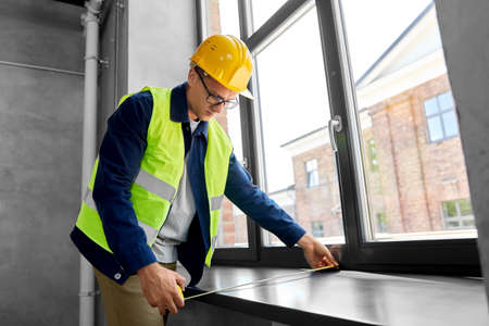 male builder with ruler measuring window sill