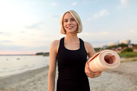 happy woman with yoga mat on beach