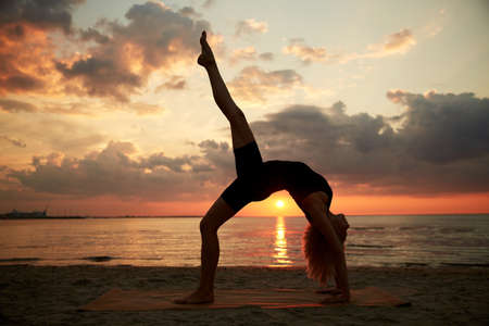 woman doing yoga bridge pose on beach