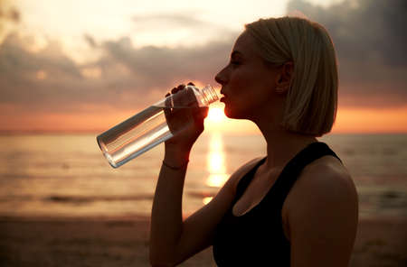 woman drinking water from bottle on beach