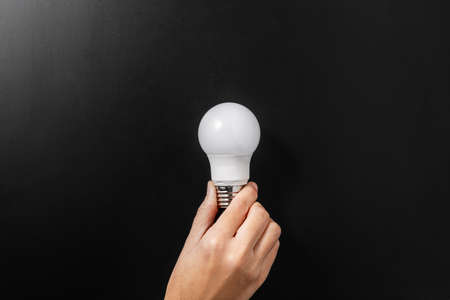close up of hand holding lightbulb over blackの写真素材