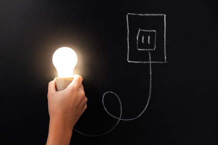 close up of hand holding lightbulb over chalkboardの写真素材