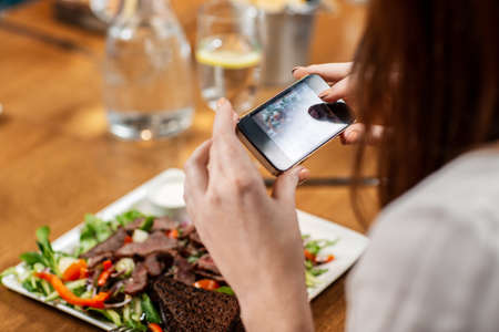 women with phone photographing food at restaurantの写真素材
