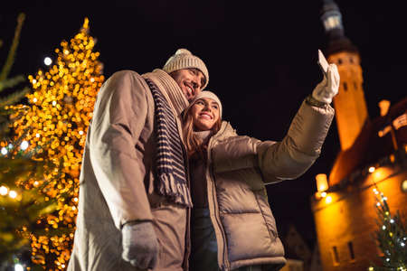 happy couple taking selfie over christmas lights