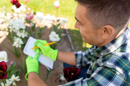 man with notebook and flowers at summer garden