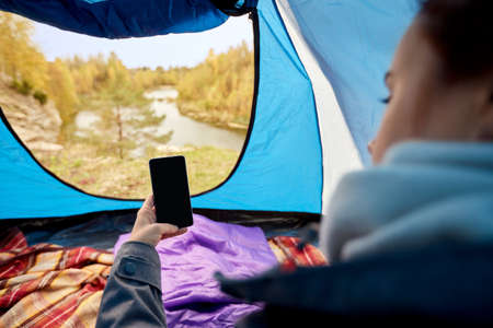 woman with phone in sleeping bag in camp tent