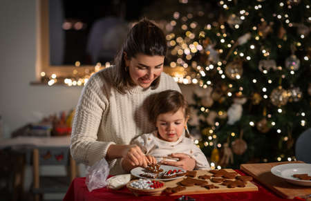 mother and daughter decorating gingerbread at homeの写真素材