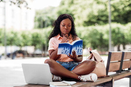 african student girl reading book in cityの写真素材
