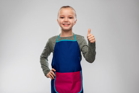 smiling little girl in apron showing thumbs upの写真素材