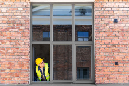 smiling male builder in helmet looking out windowの写真素材