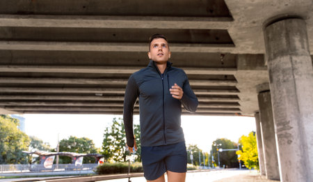 young man running outdoors under bridgeの写真素材